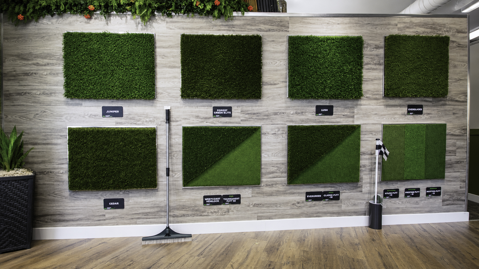 Premium Grass Blades Maple Ridge showroom wall displaying Juniper, Forest Green Elite, Lush, Everglades, Cedar, Westcoast Hemlock, Tournament Putt 50, Evergreen, Classic Putt 50, Nylon Putt, Prestige Putt, and Masters Putt turf samples